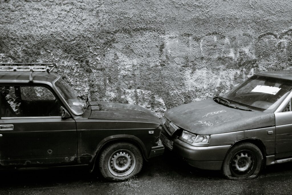 Black and white of aged automobiles with deflated tires near gray wall on street