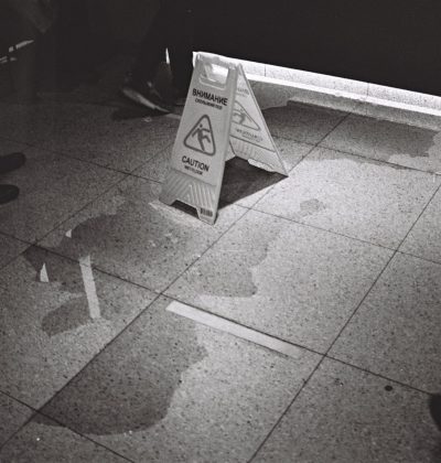 Răspundere civilă profesională Black and white image of caution sign on wet floor in indoor setting.