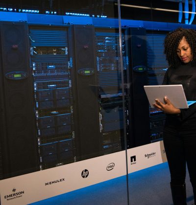 Asigurări de bunuri/clădiri PJ A female engineer using a laptop while monitoring data servers in a modern server room.
