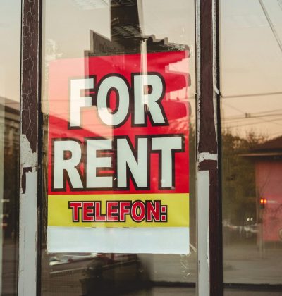 Răspundere civilă profesională Reflection of a cityscape on a window with a 'For Rent' sign and sunset glow.