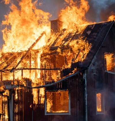 Asigurări de bunuri/clădiri PJ A house consumed by intense flames and smoke, capturing the power of fire.