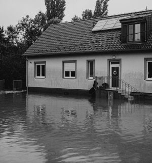 ASIGURARI LOCUINTA A monochrome image of a suburban house affected by floodwaters.