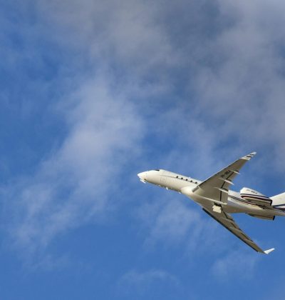 Călătorie Commercial jet airplane flying high with a clear blue sky and clouds in the backdrop.