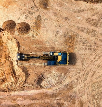 Asigurări de bunuri/clădiri PJ Aerial photo of an excavator working on a large empty construction site.