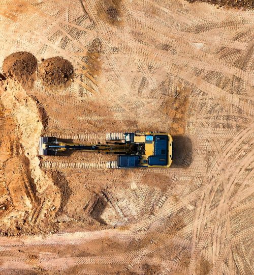 Projects Aerial photo of an excavator working on a large empty construction site.