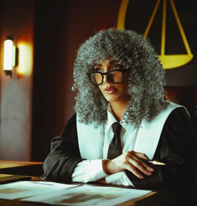 Răspundere civilă profesională Female judge in courtroom setting, sitting at desk with justice scales in background.