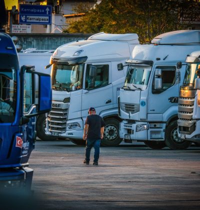 CMR/Transport Marfă A man walks among parked trucks at sunset in an industrial area, creating a serene yet busy scene.