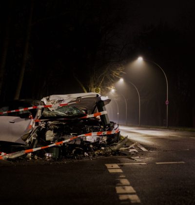 Sănătate și accidente A wrecked car after a crash on a dimly lit street in Berlin at night.