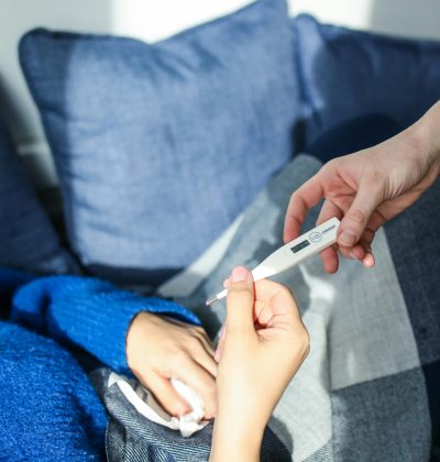Sănătate și accidente A woman checks her temperature using a digital thermometer while resting on a couch at home.