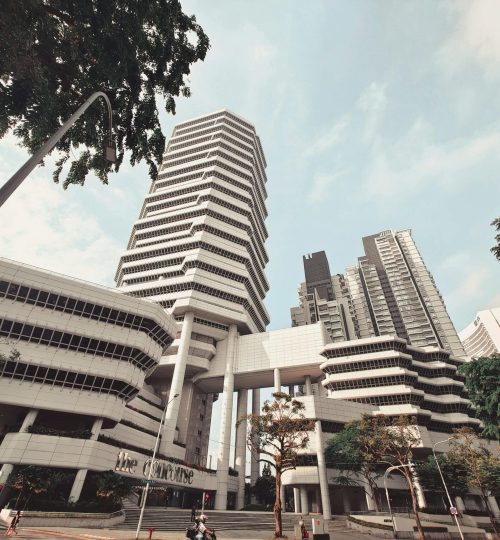 Projects Dramatic low angle view of The Concourse building in Singapore against a blue sky, showcasing modern architecture.