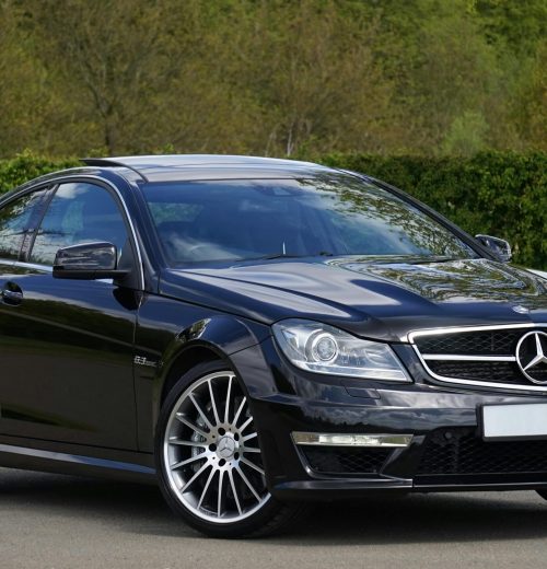 RCA Luxurious black Mercedes Benz coupe parked on a scenic outdoor setting with lush greenery.