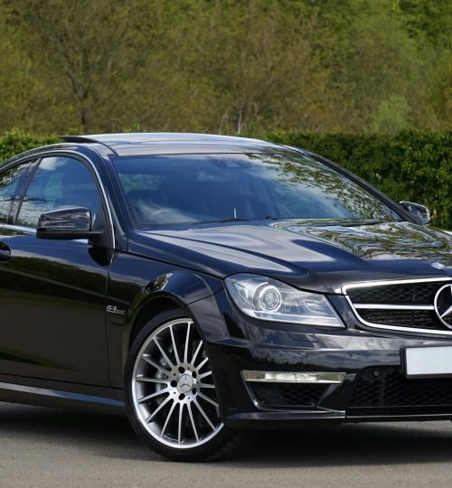 Projects Luxurious black Mercedes Benz coupe parked on a scenic outdoor setting with lush greenery.